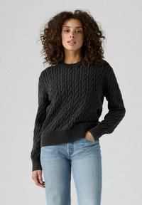 Mörkgrå kabelstickad tröja med rund hals och ribbade muddar, kombinerad med ljusblå jeans som har ett strukturerat mönster genom hela plagget.