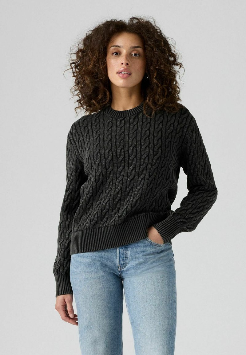 Mörkgrå kabelstickad tröja med rund hals och ribbade muddar, kombinerad med ljusblå jeans som har ett strukturerat mönster genom hela plagget.