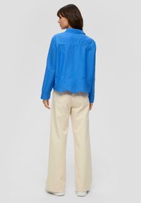 Camicia di cotone blu con collo, presenta un orlo scallop e dettagli ricamati. Abbinata a pantaloni a gamba larga color crema e sneakers bianche.