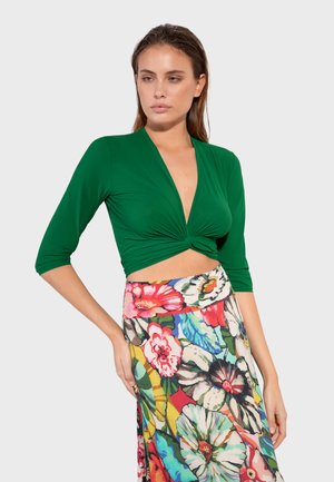 Green, fitted top with a deep V-neck and twisted front. Paired with a colorful floral midi skirt featuring varied vibrant patterns and colors.