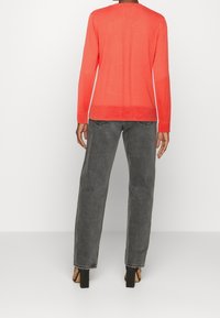 Koral långärmad tröja med rund halsringning och ribbat fåll, tillsammans med högmidjade grå denimbyxor och svarta blockklack-sandaler.