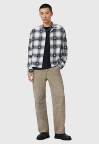 Chemise à carreaux noir et blanc à boutons avec des motifs de paix et de soleil sur un tee-shirt noir, associée à un pantalon cargo beige avec des détails de couture.