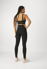 Svart sportsbh med justerbare stropper og meshdetaljer, sammen med høyhalsede sorte leggings og lysegrå joggesko med rosa detaljer.