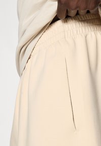 Joggeri krem boje od mekog materijala s elastičnim pojasom, s bočnim džepovima i diskretnim naborom.