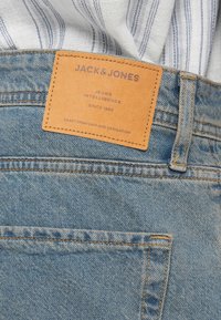 Blaue Jeans aus Denim mit einem beigen Lederetikett mit der Aufschrift "JACK & JONES", mit Stickdetails, einer fünften Tasche und einer verwaschenen Textur.