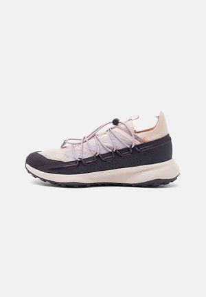 Zapatilla deportiva rosa claro y negra de corte bajo con suela gruesa, parte superior de malla y sistema de cordones elásticos con regulador sobre fondo blanco.