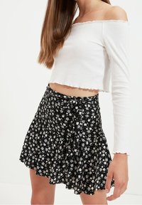 Top corto bianco a righe con spalle scoperte e bordi ondulati, abbinato a una mini gonna nera floreale con piccoli fiori bianchi e vita con fiocco.