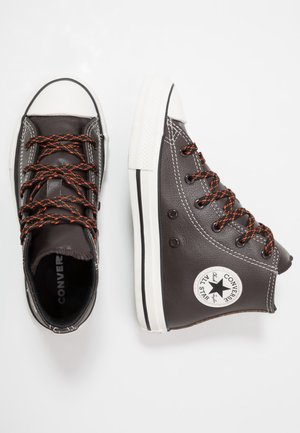 Par de zapatillas Converse All Star de cuero marrón oscuro con caña alta, suelas de goma blancas y cordones en negro y naranja sobre fondo blanco.