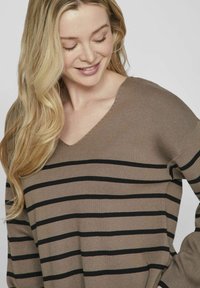 Maglione a maniche lunghe a V in beige con strisce orizzontali nere, caratterizzato da una texture a coste e una vestibilità leggermente oversize.