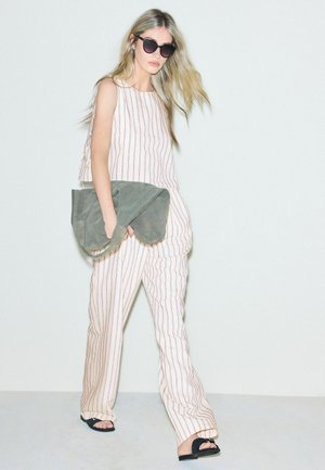 Woman wearing beige striped sleeveless top and matching pants, black sandals, sunglasses, holding large gray suede bag.