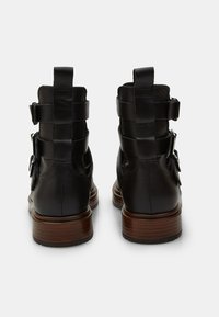 Stivaletti neri in pelle con finitura liscia, dotati di tacco in legno impilato e multiple cinghie sul retro per una calzata sicura.