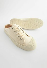 Baskets slip-on en toile beige avec lacets, semelle en caoutchouc texturé, bout rond et œillets. Design léger adapté à une tenue décontractée.