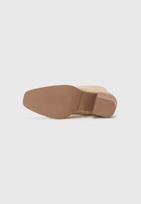 Botină bej până la gleznă, cu un exterior neted și o talpă din cauciuc texturat de culoare maro. Înălțimea tocului este moderată, având un design cu vârful rotund.