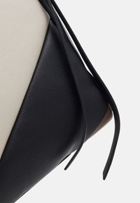 Strukturerad handväska med en kombination av svart, vitt och brunt texturerat läder, med en elegant design och långa, tunna svarta remmar.