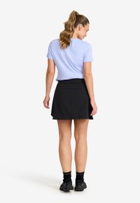 Helllila Kurzarmhemd kombiniert mit einem schwarzen Skort. Der Skort hat einen breiten Bund und ein ausgestelltes Design. Schwarze Sportsocken und -schuhe.