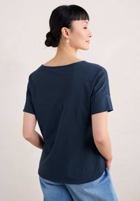 Tamno plava majica kratkih rukava s okruglim izrezom i opuštenim krojem, izrađena od mekog materijala, s glatkom teksturom i suptilnim drapiranjem.