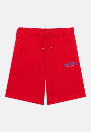 Czerwone krótkie spodenki z elastycznym pasem i sznurkiem oraz niebieskim logo "Tommy Hilfiger" na lewej nodze, pokazane na neutralnym tle.