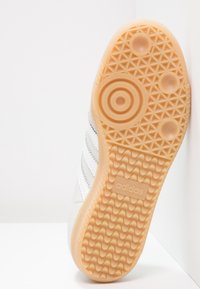 Suela de zapato con un acabado de goma texturizada en color naranja claro. Presenta un patrón circular y triangular, con un logo de adidas en el talón.