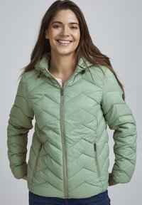 Veste matelassée verte claire avec capuche, présentant un motif en chevrons, fermeture éclair à l'avant et deux poches zippées sur les côtés.
