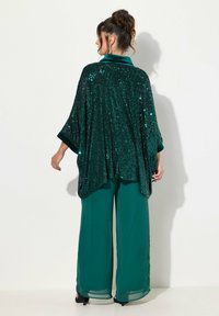 Grønne palietter poncho med løs pasform og brede ærmer, båret over matchende grønne vide bukser, der viser en glitrende tekstur.
