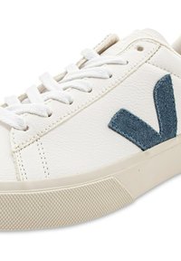 Hvide lædersneakers med et struktureret blåt suede "V"-logo. Har hvide snørebånd og en lys gummisål med et diagonalt trækmønster.