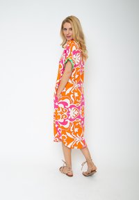 Orangenes Kleid mit weißen und rosa Blumenmustern, kurze Ärmel, knielang, mit Taschen, kombiniert mit beigen Riemchensandalen.