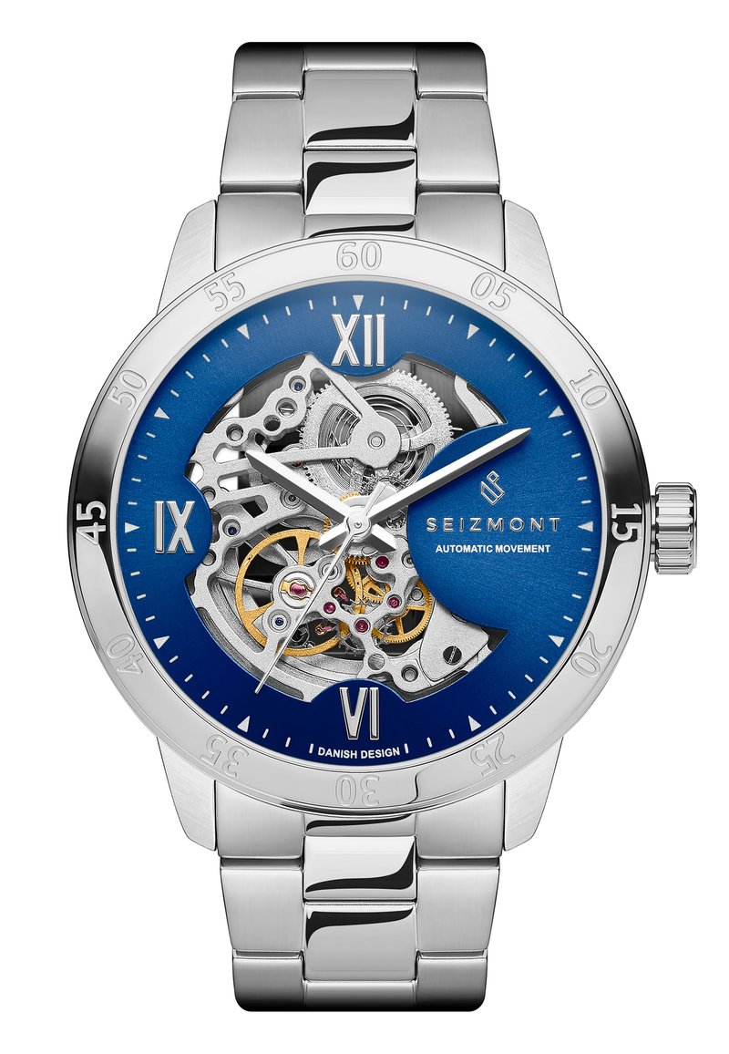 Rustfritt stål klokke med blå urskive, sølvfarget skjelettdesign, romerske tall og automatisk bevegelsesvisning. Børstet metallarmbånd.