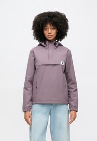 Lila vattenavvisande pulloverjacka med halvdragkedja framtill, justerbar huva och sidofickor. Har elastiska ärmslut och en logotypmärke.