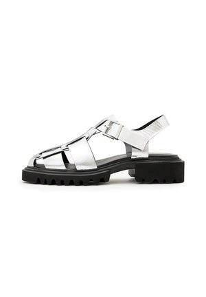 Sandalo metallico argentato con punta aperta, design con cinturini, fibbia regolabile e suola nera spessa con un motivo di battistrada testurizzato.