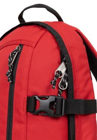 Zaino in tessuto rosso con zip nera, tracolla regolabile e fibbie. Materiale testurizzato con dettagli di cucitura a contrasto e maniglia superiore.