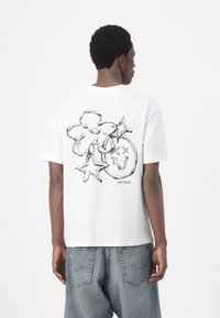T-shirt in cotone bianco con una grande grafica nera sul retro che presenta fiori e stelle. Collo a giro e vestibilità comoda.