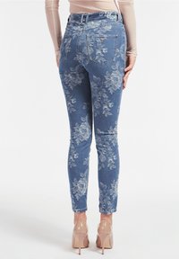 Jeans de denim azul con estampado floral, de corte ajustado, cintura alta y bolsillos traseros visibles, realzados por una textura de lavado claro.