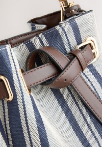 Sac en tissu rayé bleu et blanc avec des lanières en cuir marron et une boucle dorée en gros plan.