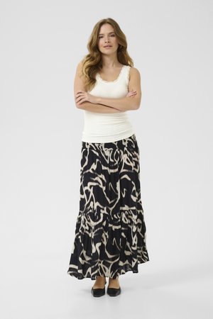 Jupe maxi à motif noir et crème avec ourlet en volants, en tissu léger, associée à un débardeur blanc ajusté et des ballerines noires.