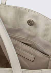 Beige schoudertas met een gestructureerde, geribbelde binnenvoering. Bevat een hoofdcompartiment, een ritsvak en een metalen drukknoopsluiting.