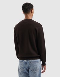Brauner, strukturierter Pullover mit einem gerippten Saum und Bündchen, getragen über hellblauen Jeans, von hinten betrachtet. Schlichtes, modernes Design.