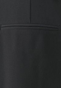 Tissu noir à la texture lisse, avec un détail cousu horizontal près du haut pour un design supplémentaire.