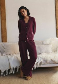 Burgundy lounge set featuring a v-neck cardigan with pockets and matching wide-leg pants. Soft fabric with subtle texture and gold-tone buttons.