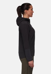 Black hoodie with a textured fabric and a zippered front, paired with olive green pants. Features long sleeves and a fitted design.