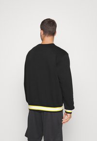 Svart sweatshirt med rund halsringning, med en gul och vit randig fåll och ärmslut. Sid sömmar synliga, med en avslappnad passform.