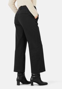 Svarta vida byxor med hög midja, sidofickor och subtila sömdetaljer, som matchas med svarta ankelskor.