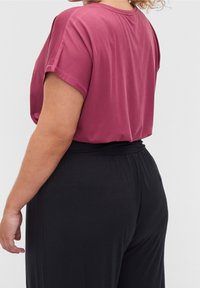 Malinowy, krótki top z luźnym krojem, zestawiony z czarnymi spodniami z elastycznym paskiem w talii. Miękka tkanina, gładka faktura, prosty design.