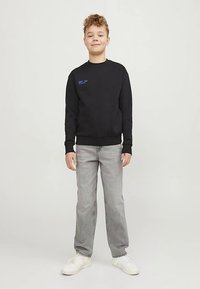 Mustapaita pyöreällä kaula-aukolla ja rintakehällä sinisellä tekstillä, yhdistetty harmaisiin farkkuihin ja valkoisiin lenkkareihin. Sileä pinta, rento istuvuus.