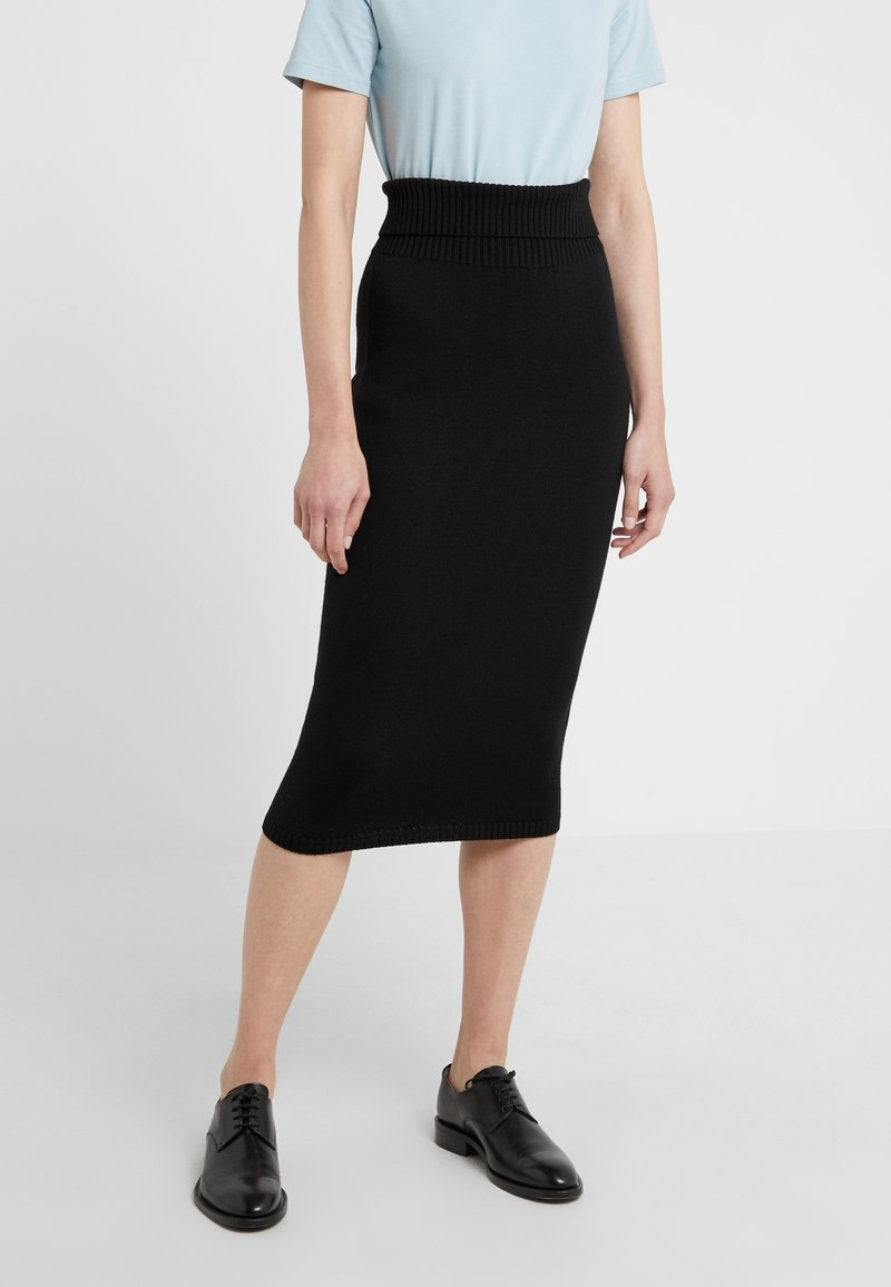 Jupe midi noire en tricot avec une taille côtelée, une silhouette fuselée et une texture lisse, associée à un haut bleu clair et des chaussures noires.