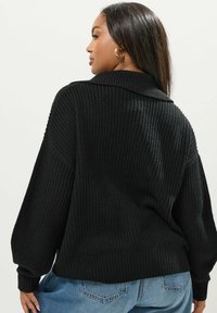 Svart stickad tröja med ribbad struktur, oversized design och krage, matchad med blå högmidjade jeans.