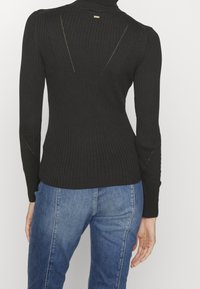 Czarny sweter z prążkowanym kołnierzem, z długimi rękawami, dopasowany fason oraz delikatnymi wycięciami na plecach, w połączeniu z niebieskimi dżinsami.
