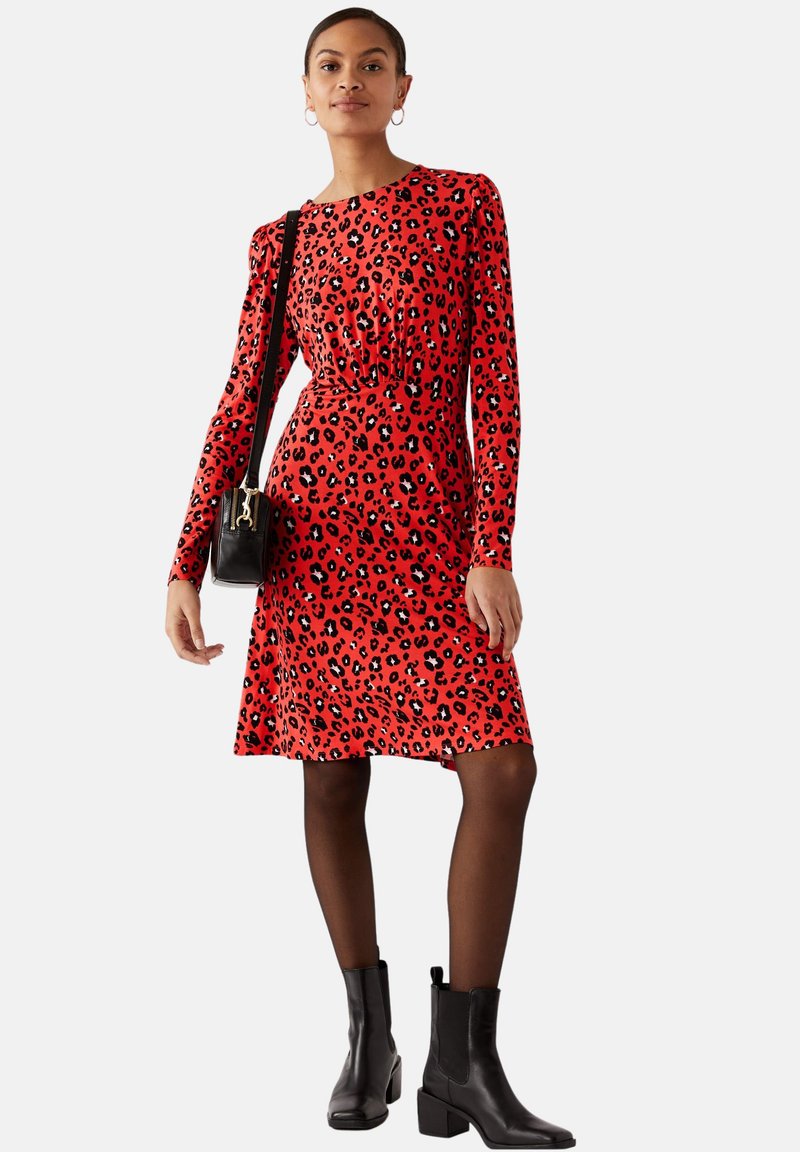 Rotes Leopardenmuster-Kleid mit langen Ärmeln, tailliertem Schnitt und ausgestelltem Rock, kombiniert mit schwarzen Stiefeletten und einer kleinen schwarzen Handtasche.