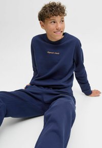 Navy blue sweatshirt and sweatpants set made of soft fabric. Sweatshirt features gold embroidered text on the chest; both have ribbed cuffs.