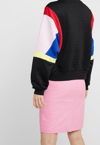 Musta collegepaita, jossa on moniväriset hihat (punainen, vaaleanpunainen, sininen, keltainen) ja ribattu helma, yhdistettynä tiukkaan vaaleanpunaiseen hameeseen, jonka linjat ovat selkeät.