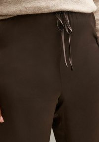 Brown, lightweight, elastic waistband pants with a textured surface and a drawstring for adjustment, showcasing a smooth, sleek design.